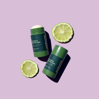 Outdoor Beauty Balm sticks with fresh lime slices on a lilac background